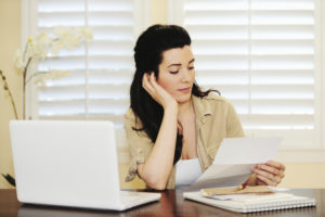 woman holding paper at desk with laptop