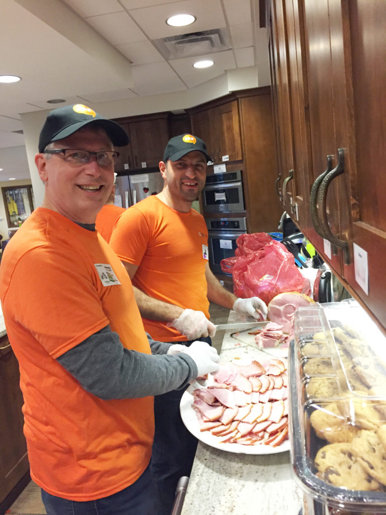 two men in orange shirts are preparing food in a kitchen
