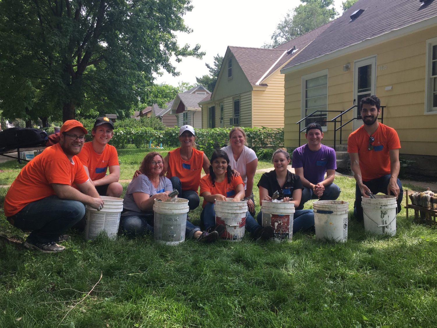 a group of people sitting in the grass with buckets of paint