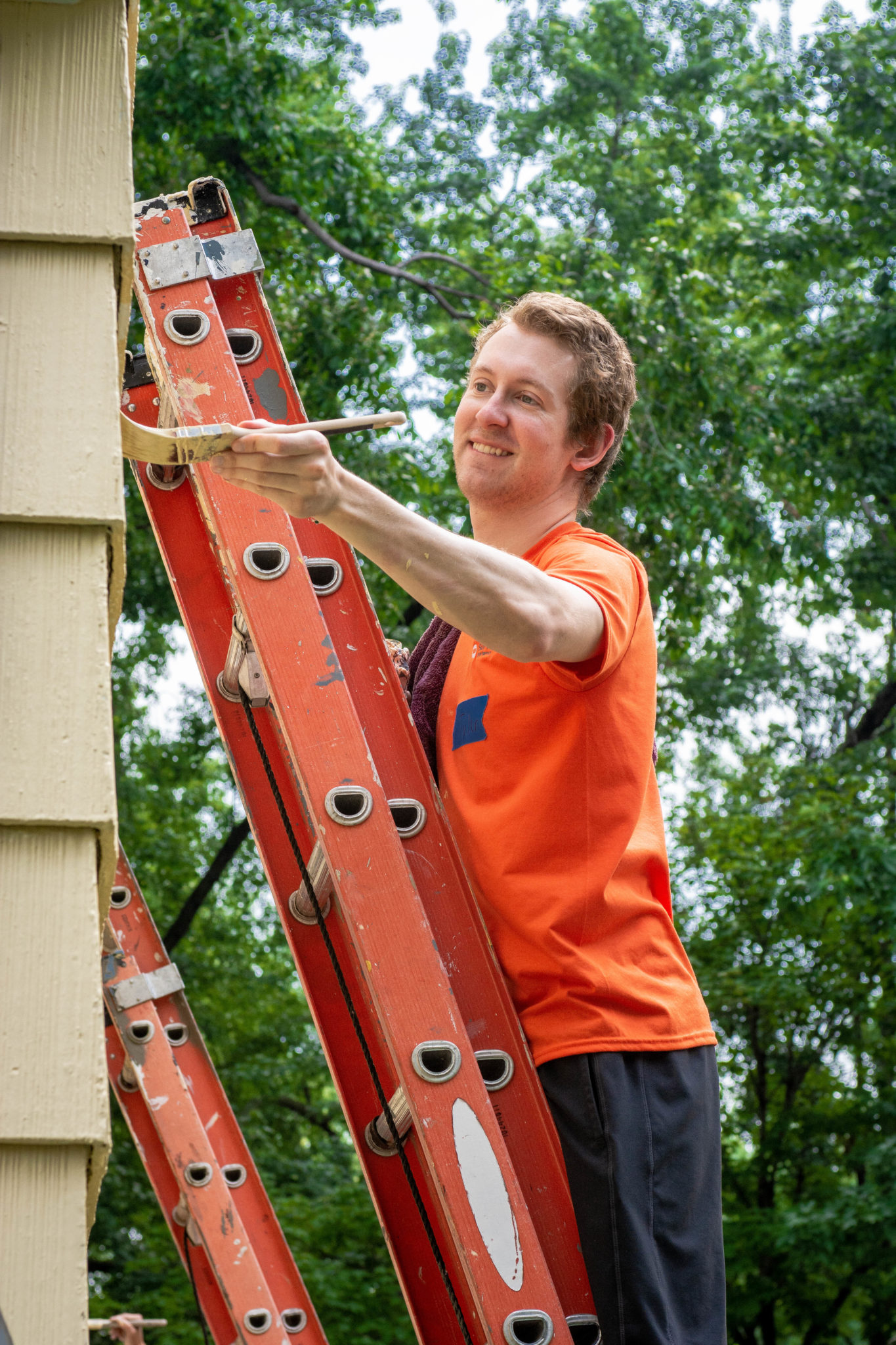 a man in an orange shirt is painting a house