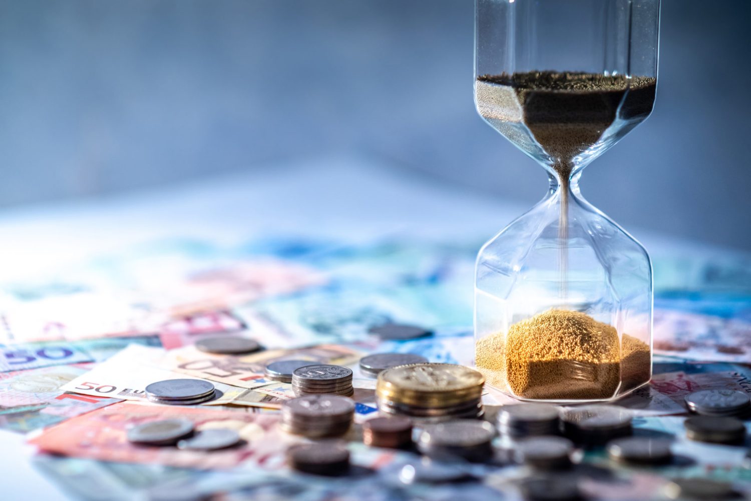 a hourglass filled with sand sits on a pile of money