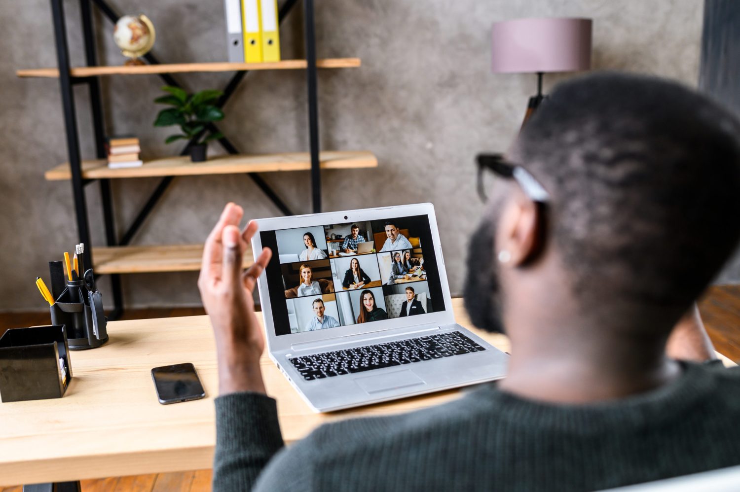Confident African-American male worker talking online with coworkers, back view of black guy speaks and gestures to many people on video screen. Remote work, virtual meeting